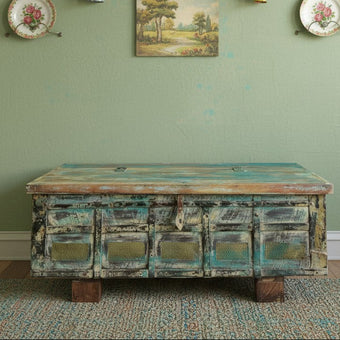 Vintage-style trunk in a room with a green wall, shelves with decorative items, and a small painting.