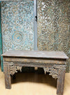 Carved wooden console with intricate patterns in front of decorative panels.
