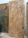 An ornate carved wooden panel with floral and bird motifs, standing upright next to another painted wooden pane 
