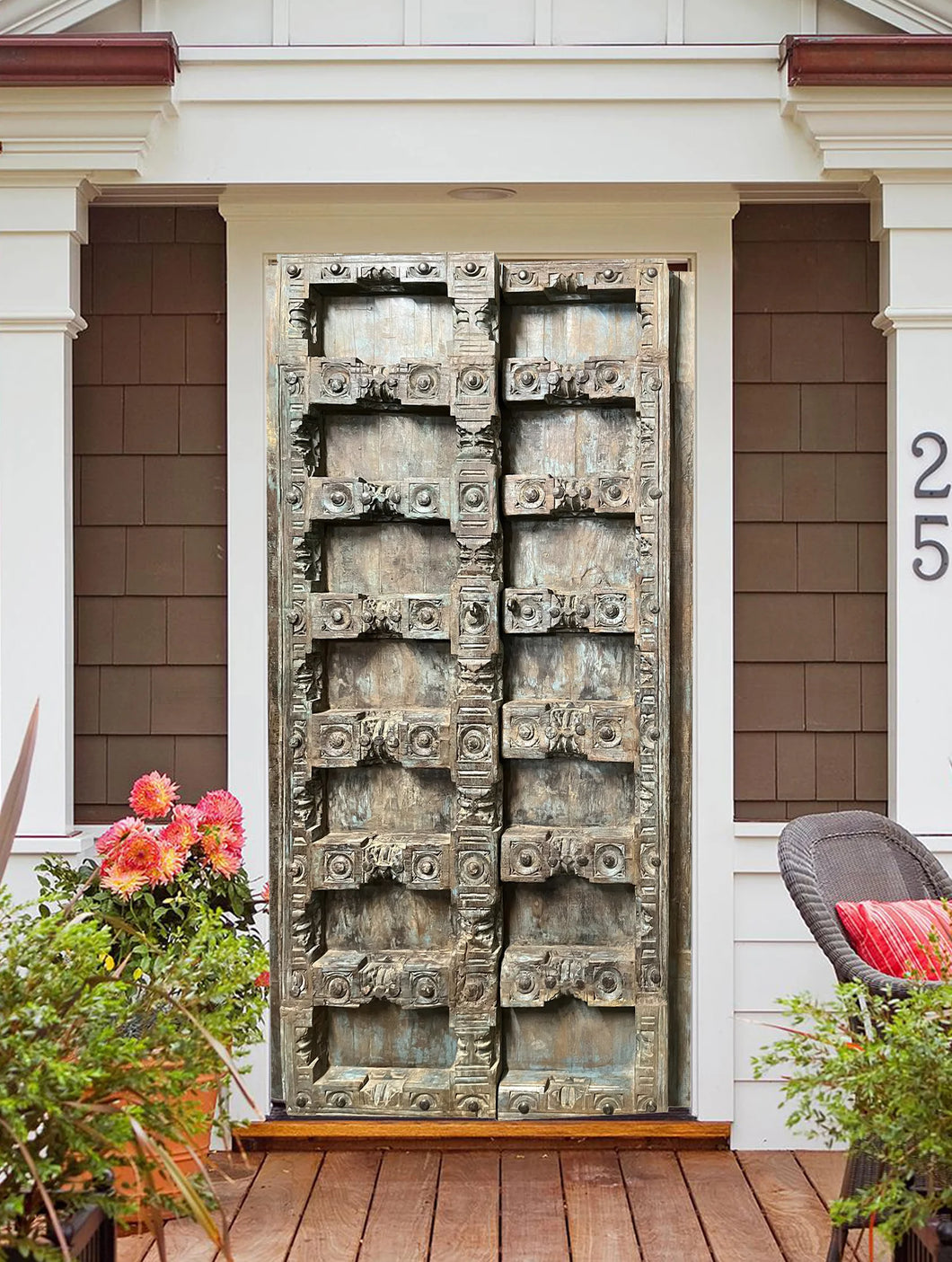  Decorative metal gate on a house exterior with flowers and a chair in the foreground.